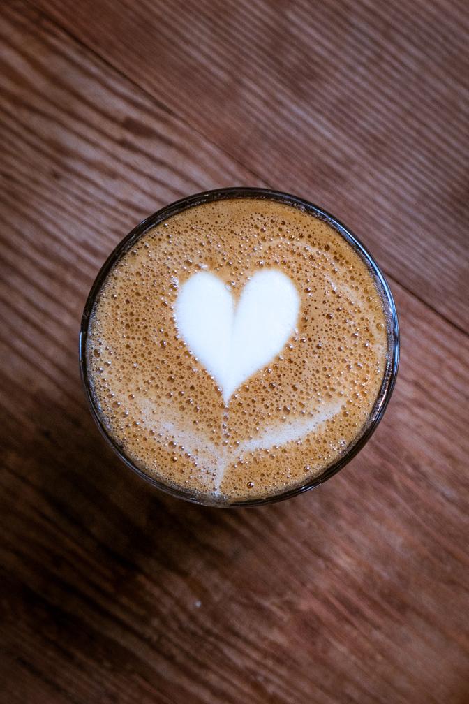 A latte sitting on a wooden table with a milk heart